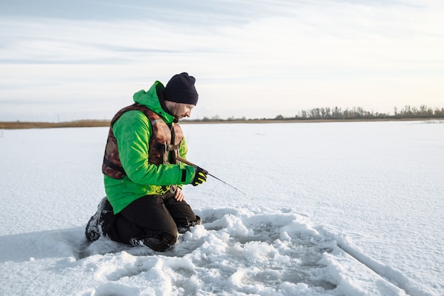 Jeune homme lors d'un voyage de pêche d'hiver sur un lac enneigé poissons sur une canne à pêche