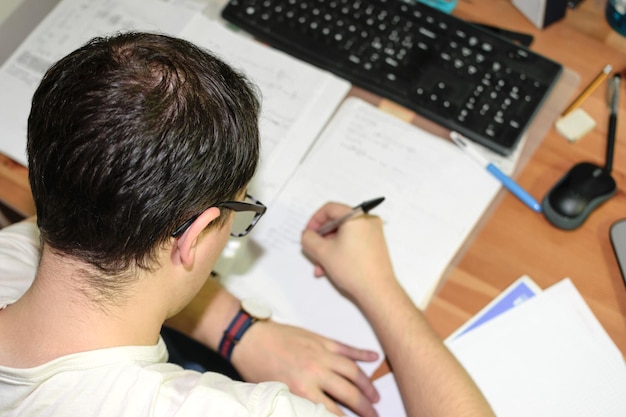Jeune homme à lunettes étudiant concentré à son bureau avec son ordinateur