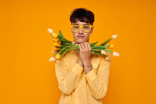 Un jeune homme à lunettes jaunes avec un bouquet de fleurs de vacances inchangé