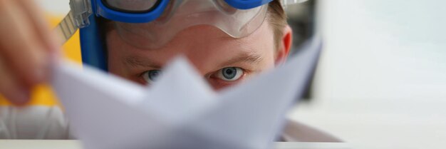 Un jeune homme avec des lunettes de natation joue avec un navire en papier sur le lieu de travail