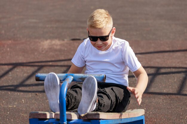 Un jeune homme à lunettes noires entraîne les muscles de la presse sur le terrain de sport en été. photo de haute qualité