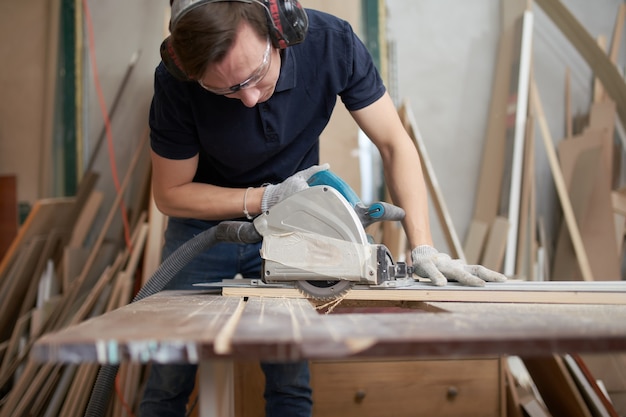 Jeune homme en lunettes de sécurité et gants blancs travaille sur un puzzle en atelier