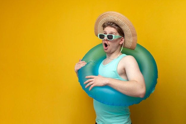 Un jeune homme à lunettes de soleil et avec un anneau de bain gonflable en été en vacances montre une surprise