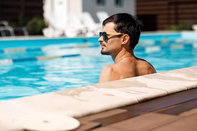 Jeune homme à lunettes de soleil dans la piscine