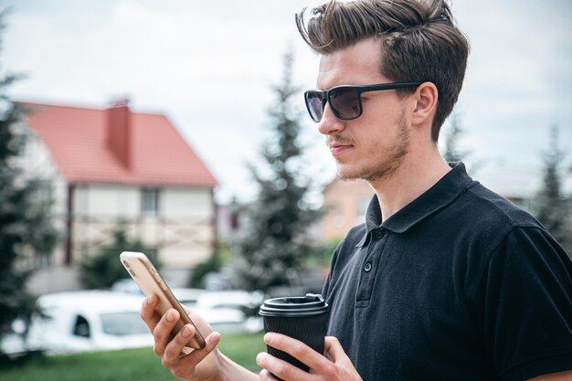 Un jeune homme à lunettes de soleil avec smartphone et café dans la ville