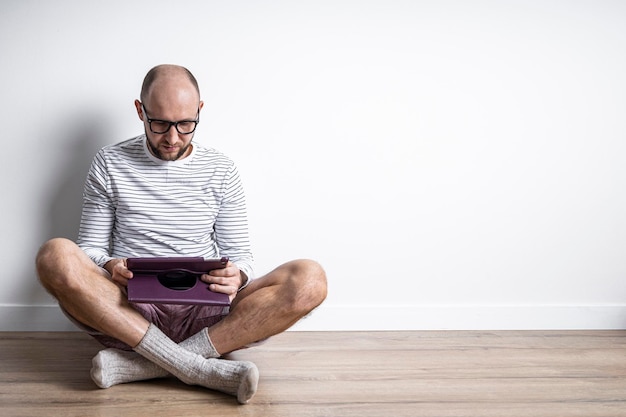 Jeune homme à lunettes avec une tablette assis sur le sol