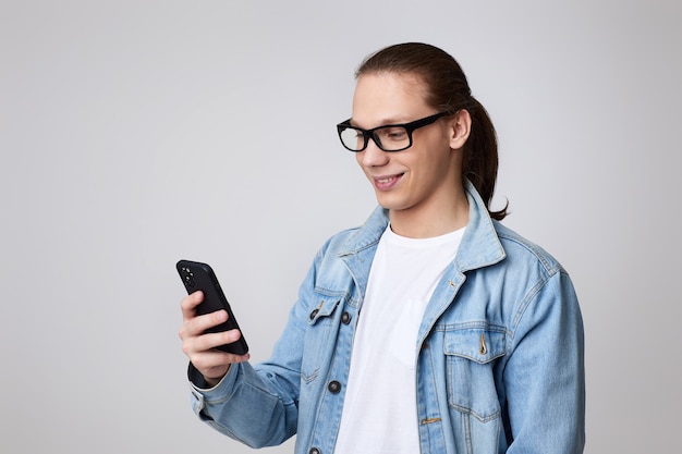 Jeune homme à lunettes et veste jeans à l'aide de smartphone