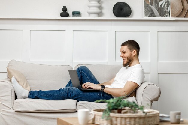 Jeune homme à la maison sur un canapé avec un ordinateur portable