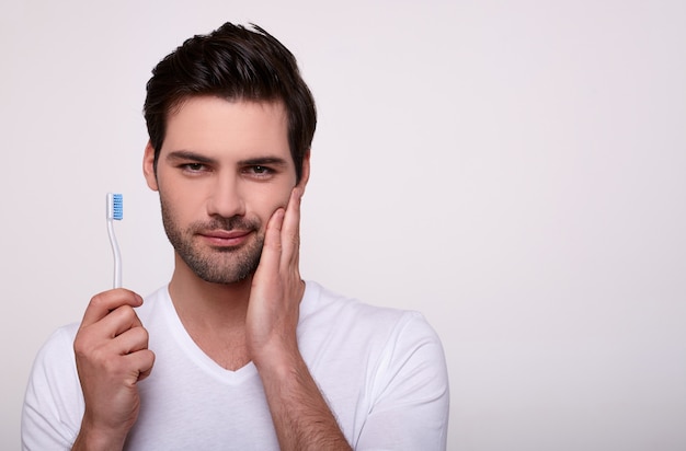 Un jeune homme avec un mal de dents tient une brosse à dents à la main.