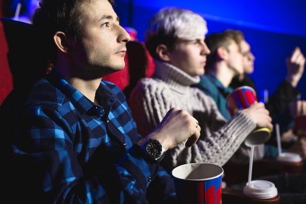 Un jeune homme mange du pop-corn au cinéma et regarde un film.