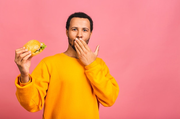 Jeune homme mangeant un hamburger isolé sur rose