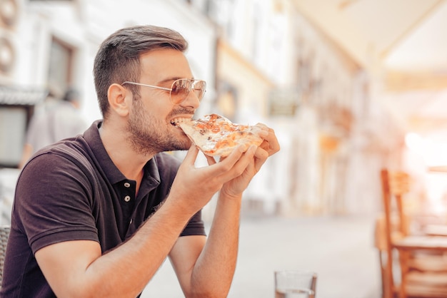 Jeune homme mangeant une tranche de pizza