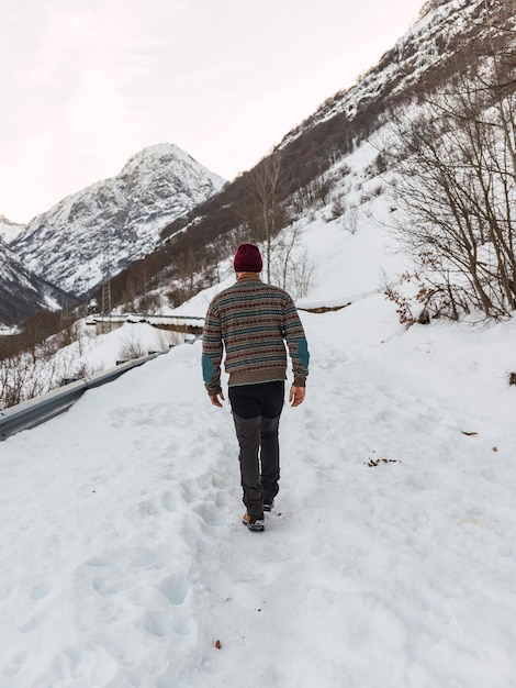 Jeune homme marchant dans la neige vêtu de vêtements d'hiver dans les montagnes enneigées des Alpes italiennes.