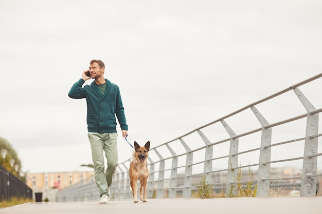 Jeune homme marchant avec son chien le long de la rue et parler au téléphone mobile