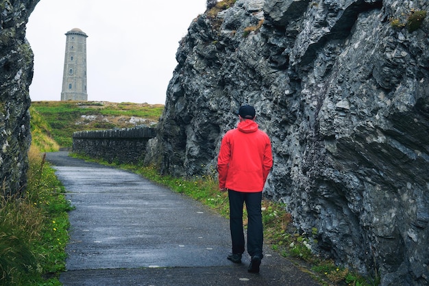 Jeune homme marchant vers le phare de Wicklow Head en Irlande