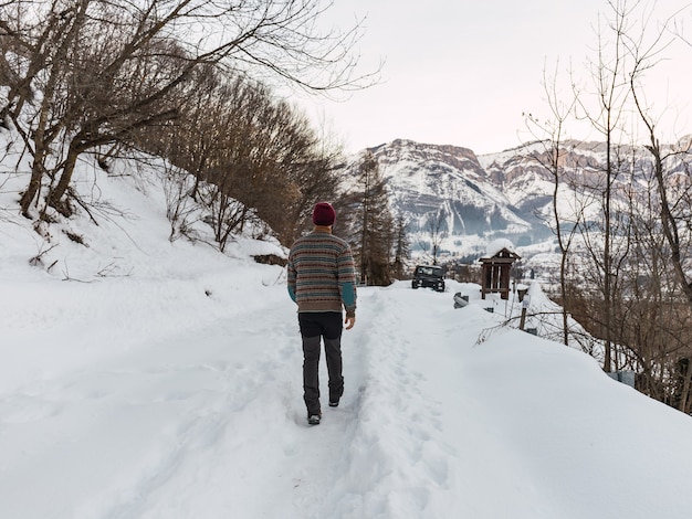 Photo jeune homme marchant vers une voiture tout-terrain dans la neige en vêtements d'hiver dans les montagnes des alpes italiennes.