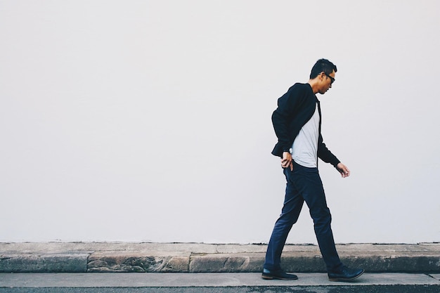 Un jeune homme marche dans la rue contre un mur blanc.