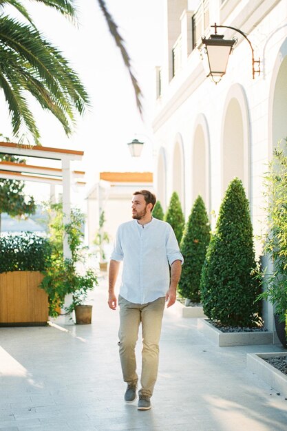 Un jeune homme marche dans la rue devant un bâtiment avec des arches et des arbres tubulaires