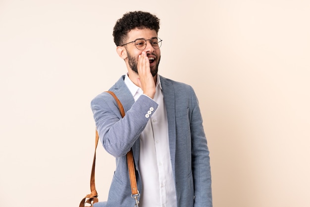 Jeune homme marocain d'affaires isolé sur fond beige en criant avec la bouche grande ouverte sur le côté