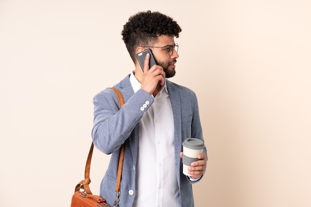 Jeune homme marocain d'affaires isolé sur fond beige tenant du café à emporter et un mobile