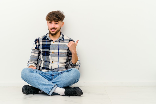 Jeune homme marocain assis sur le sol choqué de pointer avec l'index