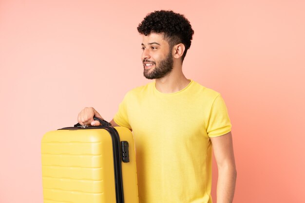 Jeune homme marocain isolé sur rose en vacances avec valise de voyage