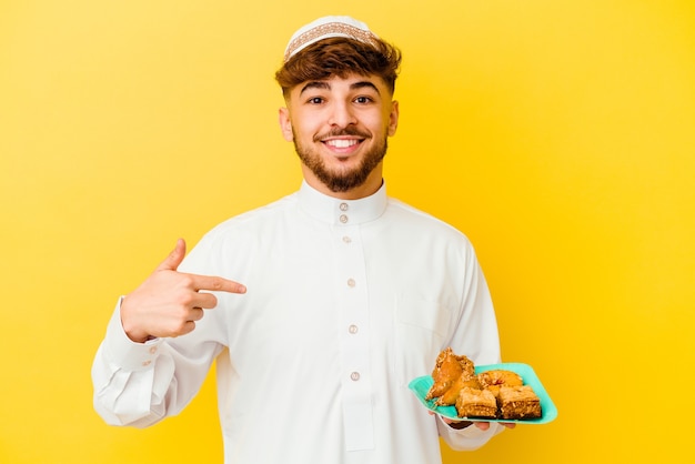 Jeune Homme Marocain Portant Le Costume Arabe Typique De Manger Des Bonbons Arabes Isolé Sur Fond Jaune Personne Pointant à La Main Vers Un Espace De Copie De Chemise, Fier Et Confiant