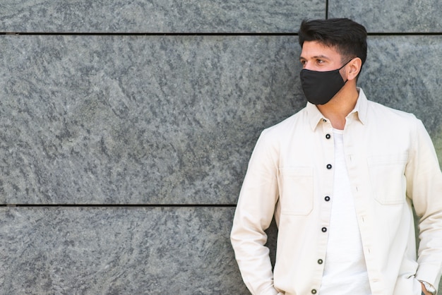 Jeune homme avec masque covid ou coronavirus appuyé contre un mur dans une ville
