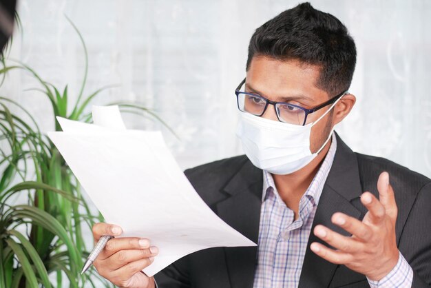 Jeune homme avec masque facial lisant quelque chose sur un papier