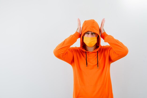 Jeune homme avec un masque orange couvrant ses oreilles avec les mains sur fond blanc