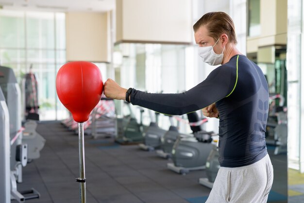 Jeune homme avec un masque pour se protéger de la boxe contre l'épidémie de coronavirus au gymnase pendant le coronavirus Covid-19