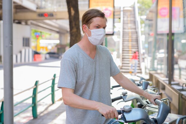 Jeune homme avec masque vélo de stationnement à la station de service de vélos publics