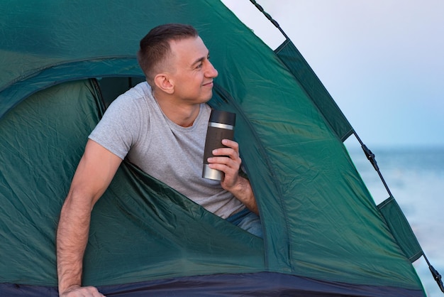 Jeune homme le matin dans une tente avec une tasse touristique dans ses mains Camping Tourisme actif