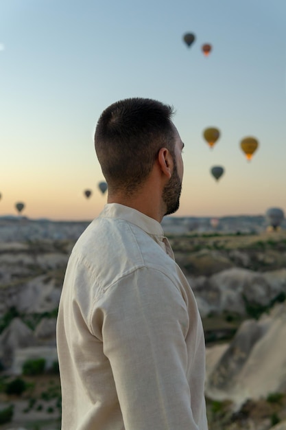 Jeune homme méconnaissable au premier plan profitant de la vue sur les montgolfières volant au lever du soleil en Cappadoce Turquie