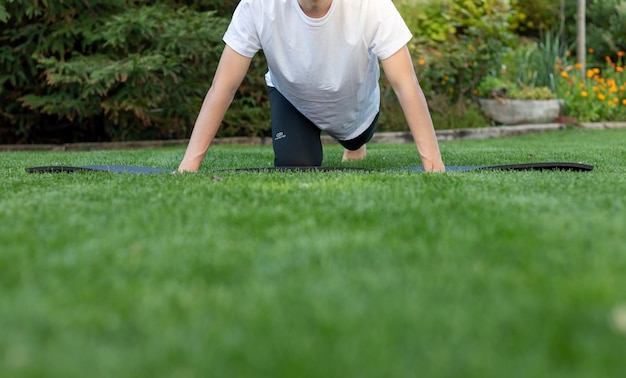 Jeune homme méconnaissable faisant de l'exercice dans le jardin sur un tapis de yoga en temps de sprint