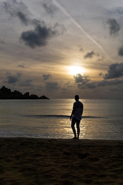 Jeune homme méconnaissable regardant le coucher du soleil sur le rivage de la plage
