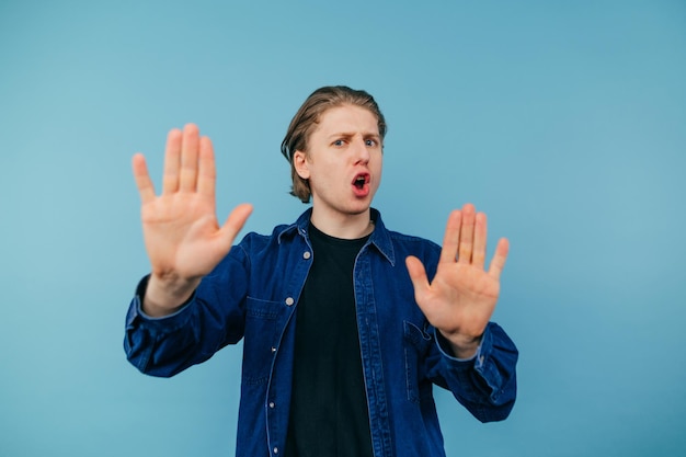 Le jeune homme mécontent dans une chemise se tient sur un fond bleu regarde l'appareil-photo