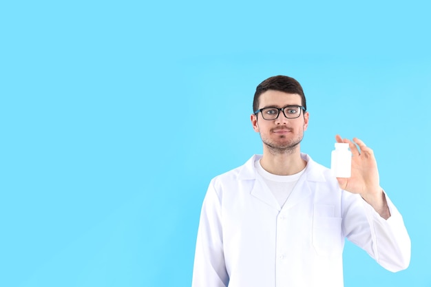 Jeune homme médecin détient une bouteille de pilules sur fond bleu