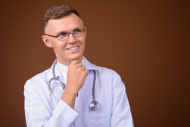 Jeune homme médecin portant des lunettes sur fond marron