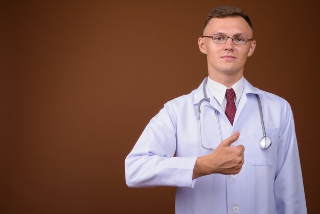 Jeune homme médecin portant des lunettes sur fond marron