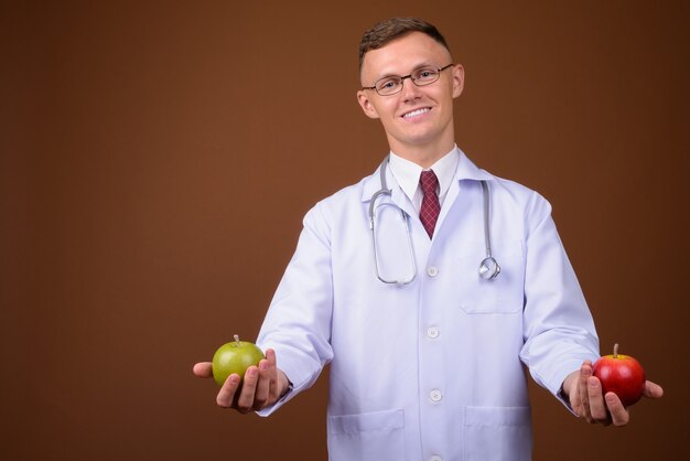 Jeune homme médecin portant des lunettes sur fond marron