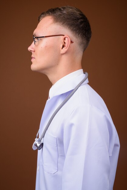 Jeune homme médecin portant des lunettes sur fond marron