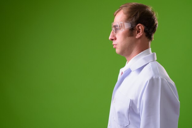 Jeune homme médecin portant des lunettes de protection contre le mur vert