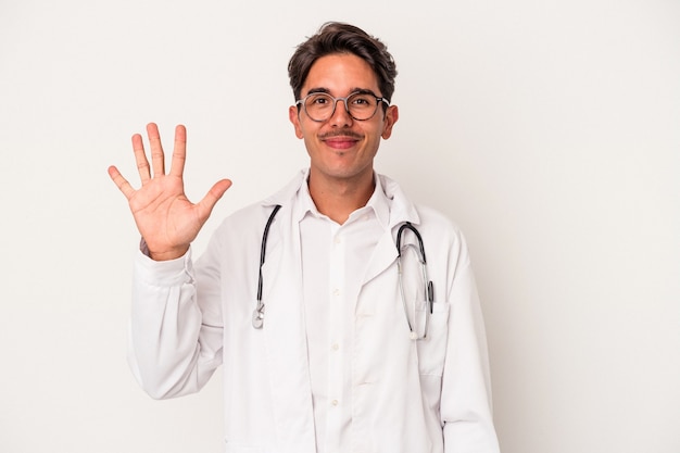 Jeune homme médecin de race mixte isolé sur fond blanc souriant joyeux montrant le numéro cinq avec les doigts.