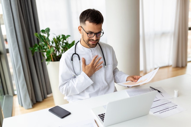 Jeune homme médecin travaillant à son bureau faisant des services de télémédecine Aider les patients en ligne et par téléphone Consultations de soins primaires