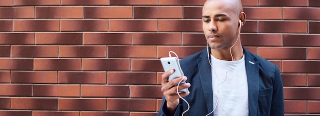 Jeune homme mélomane portant des écouteurs debout sur le mur écoutant de la musique sur un smartphone sérieux