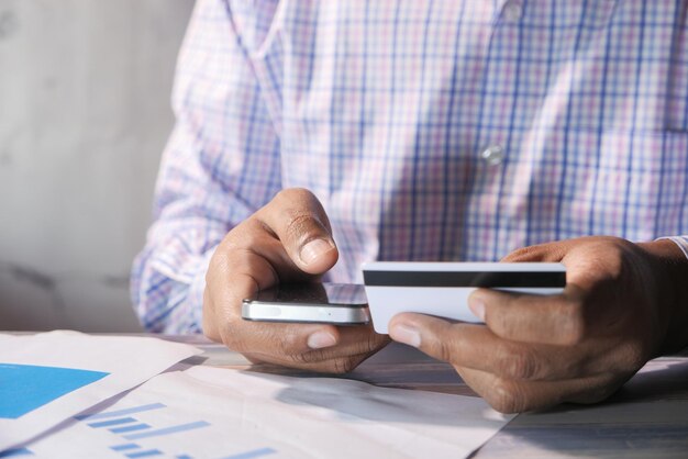 Jeune homme mettant les détails de la carte de crédit sur un téléphone intelligent