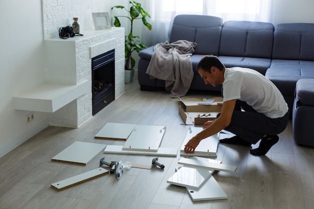 jeune homme mettant des meubles à monter soi-même alors qu'ils emménagent dans votre nouvelle maison.