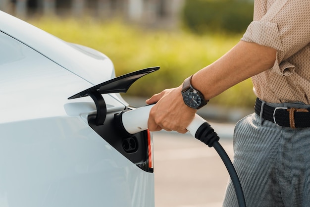 Un jeune homme a mis un chargeur EV pour recharger la batterie de la voiture électrique à partir d'une station de recharge dans un parking commercial de la ville. Voiture EV rechargeable pour un déplacement urbain durable et respectueux de l'environnement.