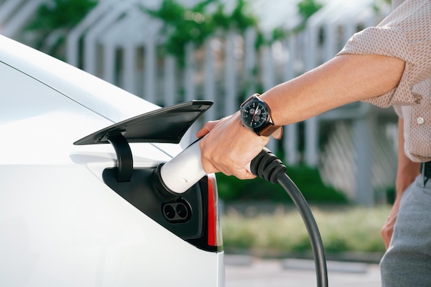 Un jeune homme a mis un chargeur EV pour recharger la batterie de la voiture électrique à partir d'une station de recharge dans un parking commercial de la ville. Voiture EV rechargeable pour un déplacement urbain durable et respectueux de l'environnement.